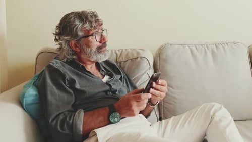 Senior Man Relaxing on Couch with Mobile Phone