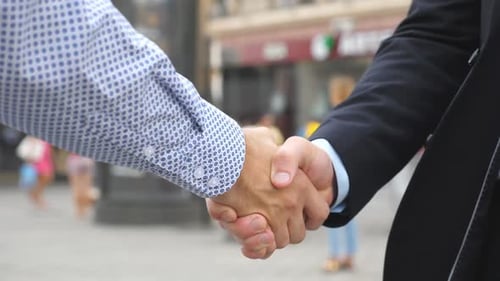 Two Young Male Colleagues Shaking Hands with Blurred City Background Confident Businessmen Greeting