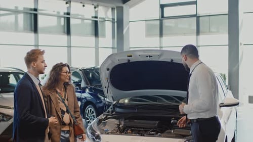 Male Sales Manager Demonstrating Car Engine to Couple in Showroom