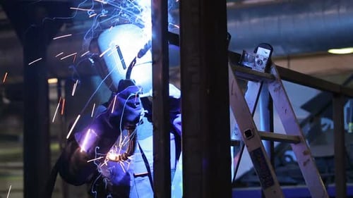 Weld Of Steel Detail Indoors The Plant Close Up. Man Working In Gloves And Protective Wear, Helme...