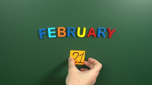 Hand sticking a sticker 21 February calendar day on school board. 21 date of February. Twenty first