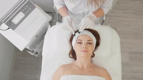 A Beautiful Woman Receives a Microcurrent Facial Skin Treatment From Cosmetologist in a Spa Salon