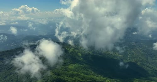 Flying trough white fluffy clouds above green mountain peaks. Beautiful summer sunny day on the high