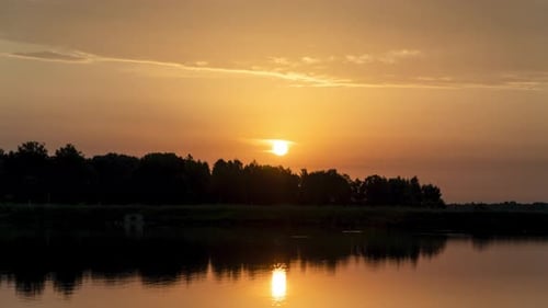 Timelapse. Sunrise on the lake, the sun rises from the trees and goes into the clouds.