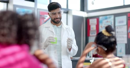 In a school classroom, a young biracial teacher demonstrates a chemistry experiment