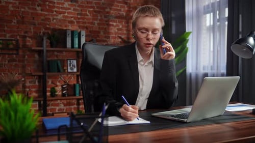 Focused Professional Writing Notes in Modern Office and Talking on Phone