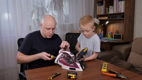 A Man Teaches a Little Boy How to Repair an Iron with a Screwdriver at Home