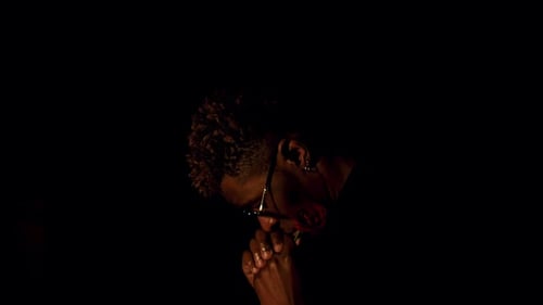 Homme noir inclinant la tête sur les mains croisées demandant pardon dans le noir, vue de profil