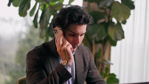 a serious man a businessman works at a laptop in the office communicates with colleagues smartphone