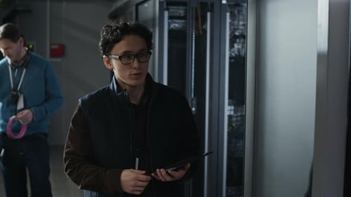 Network Engineer Inspecting Server Rack with Tablet in Data Center
