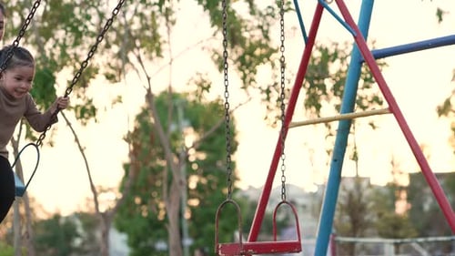 slow motion of cheerful child girl with mother playing on a swing at playground