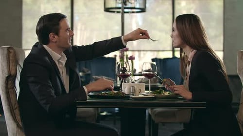 Romantic Couple Eating At Restaurant. Man Giving Food To Woman At Romantic Dinner. Happy Couple D...