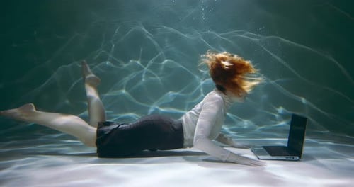 Filmaufnahme einer jungen rothaarigen Geschäftsfrau, die ihren Laptop unter Wasser benutzt, um Kunden beim Schwimmen zu beraten