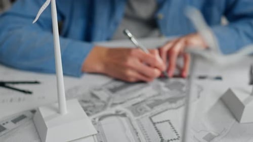 Person creating a wind energy model design on a blueprint with mini wind turbines displayed
