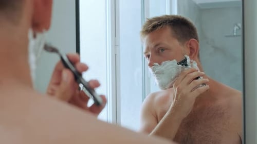 Caucasian Handsome Yong Man with Shaving Foam on His Face While Shaving His Beard Standing in the