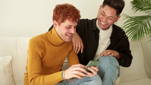 Gay Couple Sitting on the Sofa Using a Mobile Phone
