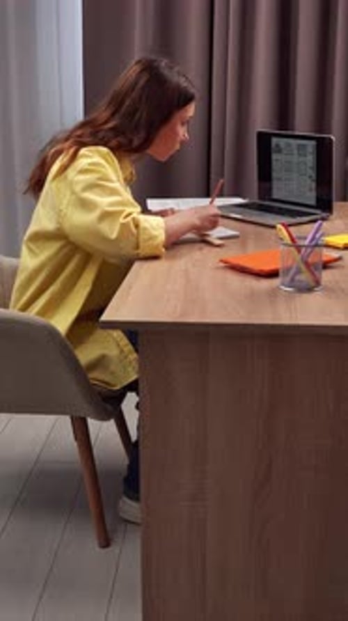 Young Woman Studying at Home Using Laptop and Taking Notes