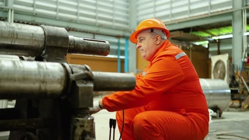 Senior male engineer operates a heavy-duty industrial metal rolling machine in a factory
