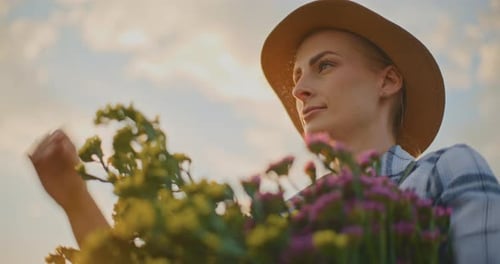 Young Woman Holding Flowers in Field at Sunset