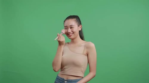 Beautiful Asian Woman Rouging Her Cheeks And Smiling To Camera On Green Screen Background