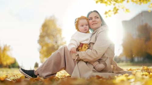 Mother Holding Baby Girl in Autumn Park Under Warm Golden Sunlight