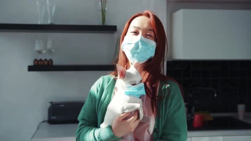 Young Calm Asian Woman with Chihuahua Dog Standing in the Kitchen Both Wearing Protective Medical
