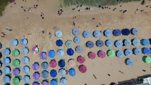 Drone footage showing rows of vibrant parasols on a sunny tropical beach,