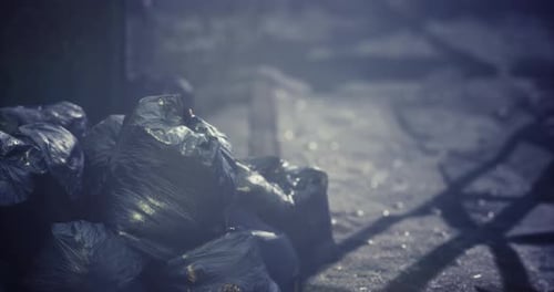 Discarded Trash Bags Stacked on a Dimly Lit Street at Night