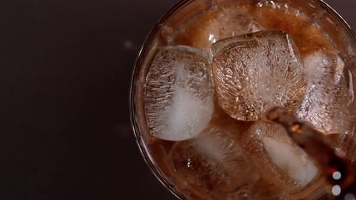 Pouring cola drink with ice cubes close-up.