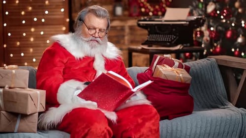 Santa Claus in Red Costume Reading Fairy Book List of Childish Wishes and Xmas Gifts at Home