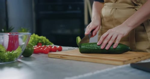 Close up woman cutting fresh cucumber on cutting board while preparing vegetable salad