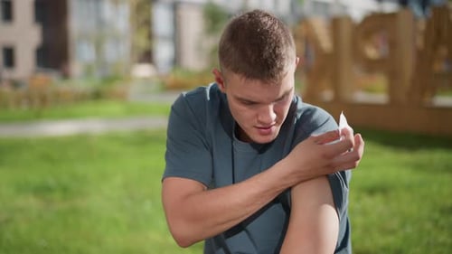 Young Boy Applying Nicotine Patch on Upper Arm Outdoors with Green Blur Background