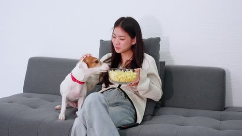 Woman Eating Popcorn and Petting Dog on Couch