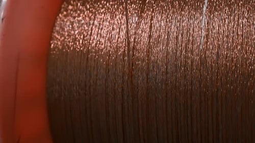 Close-up of rotating coil with copper wire. Creative. Bobbin rotates and winds copper wire.