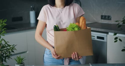 Young woman holding paper package with food that she bought in food store and looking at camera