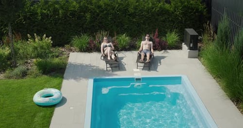Young Couple Relaxing By the Pool Lying on Sun Loungers and Sunbathing