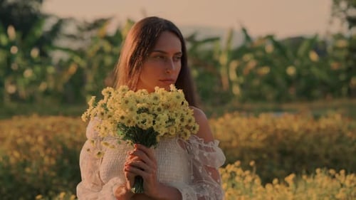 A Woman Embraces Beautiful Yellow Flowers in a Serene Field During a Sunset Glow