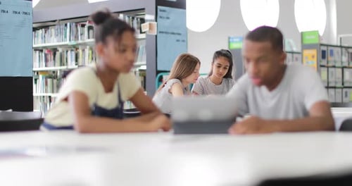 High school students studying together in a library with a digital tablet