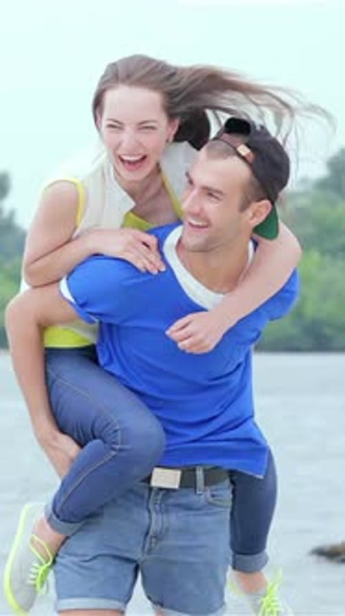 Joyful Girl springt auf den Rücken eines Mannes, während sie in Zeitlupe spielerisch am Strand entlang rennen