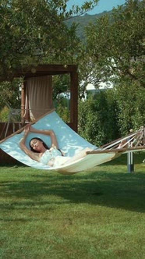 Young woman relaxing in a hammock in a lush green garden on a sunny day