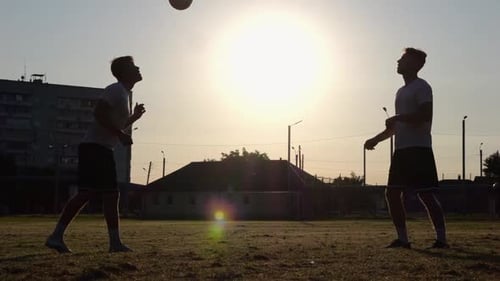 Silhouette of Professional Footballers Kicking Soccer Ball with Their Heads on Stadium at Sunset Two