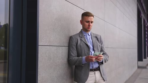 Man Leaning on the Wall of the Building Holding Money Real Time