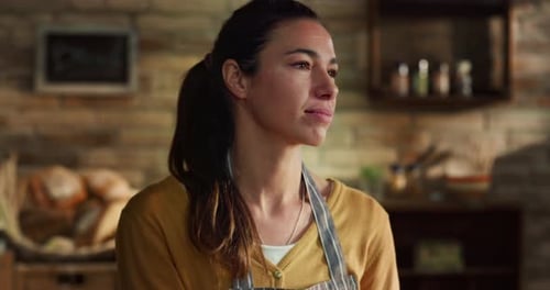 Cinematic close up shot of young female artisan baker is looking out of window and smiling while k