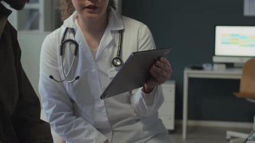 Doctor Reviews Tablet with Patient in Medical Office