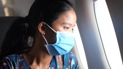 Young Woman Wearing Mask on Airplane Looking Out Window