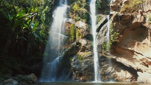 Majestic Tropical Waterfall Cascading Over Rocky Cliffs Surrounded By