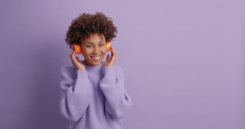 Optimistische lockige Frau bewegt sich sorglos vor lila Hintergrund und genießt Lieblingsmelodiefänge