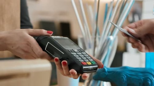 Young woman works at restaurant cash desk as man pays with card in slow motion