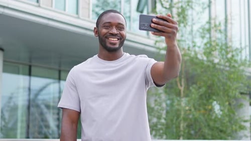 African American Man Holding Smartphone Having Video Chat on Urban Street in City Guy Blogger