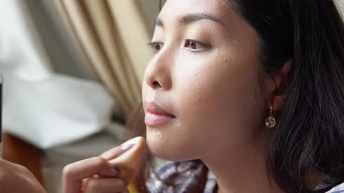 Close up portrait of beautiful young Asian woman applying make up using make up brush and puff